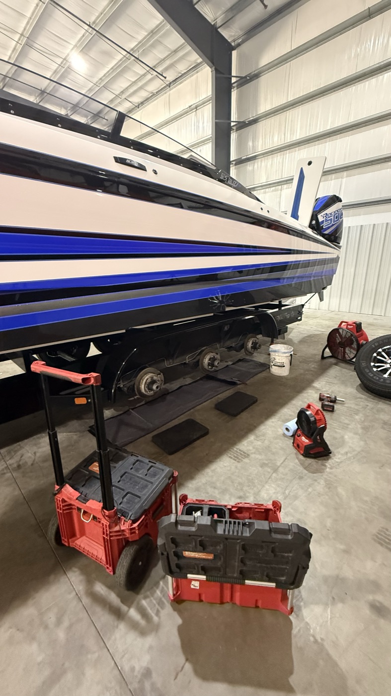 Hub and brake work on a triple-axle trailer under a performance boat, tools set up alongside